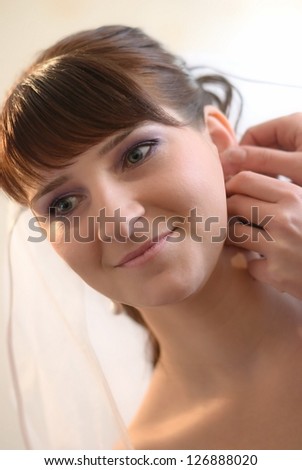 The bride smiles. To the bride help to put on an earring