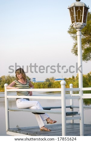 The girl sits on a pier and looks afar