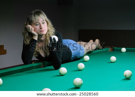 The girl lays on a billiard table and looks on the ball