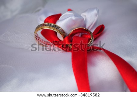 Gold wedding rings on a satiny pillow with red tapes