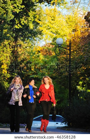 Three girls walk on park. They talk and smile