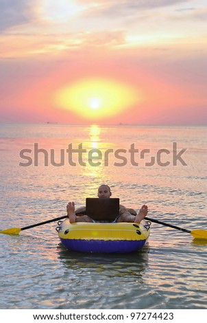 guy in a boat with a laptop swims in the sea at sunset