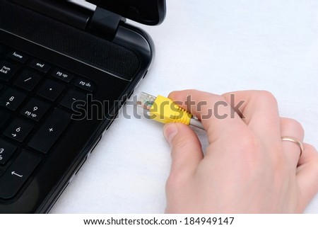 Man\'s hand connects the cable to the laptop