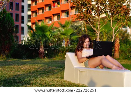 Girl lying on a deck chair and working on a laptop