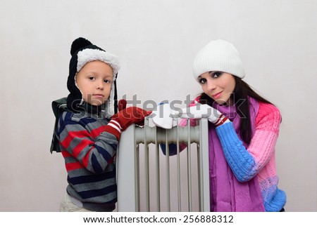Mom and boy in mittens and hats bask near radiator