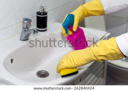 Woman doing chores in bathroom, cleaning sink and faucet with spray detergent. Cropped view
