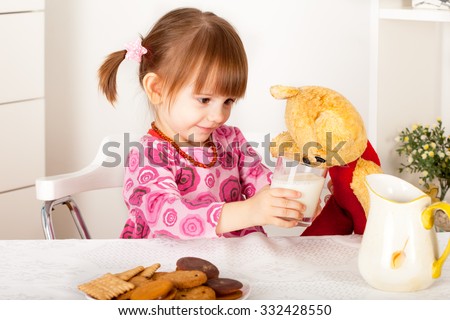 Little girl giving glass of milk to teddy bear