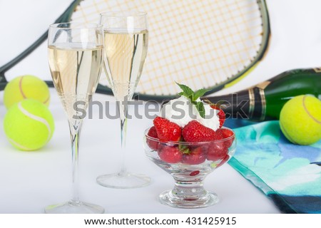 Strawberries with whipped cream and champagne, tennis racket and balls on table in background