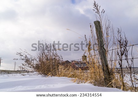 The old fence line with rural country farmhouse in the snowy background.