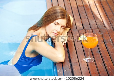 Relaxed elderly woman resting at edge of swimming pool with cocktail