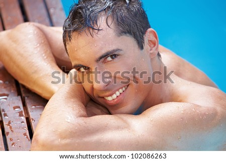 Smiling happy attractive man in swimming pool with blue water