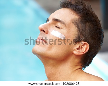 Attractive man sunbathing near pool with sunscreen on his face