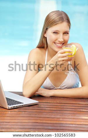 Attractive smiling woman with cocktail and laptop in swimming pool