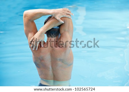 Young man doing back exercises in blue water in swimming pool