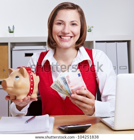 Happy winning woman with piggy bank and Euro money at desk in office