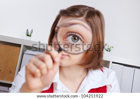 Woman in office looking through magnifying glass with her eye
