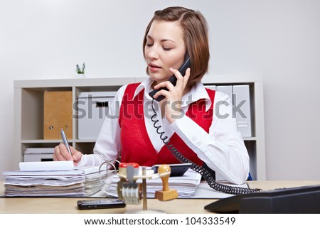 Secretary in business office taking notes while talking on the phone