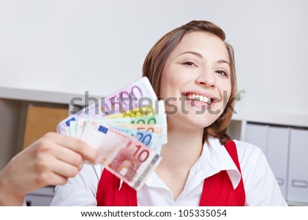 Smiling happy woman with Euro money fan sitting at her desk in the office