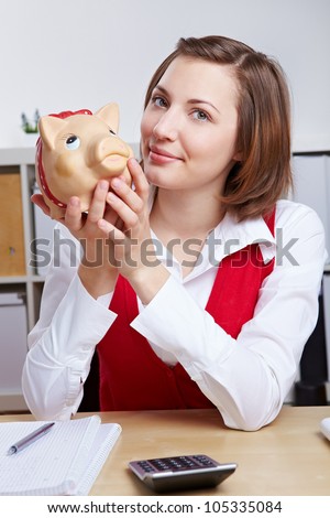 Attractive smiling business woman with piggy bank at her desk