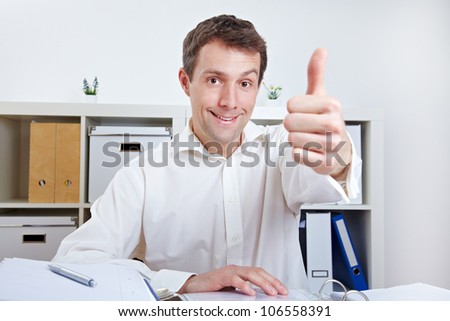 Happy business man holding thumbs up at his desk in the office