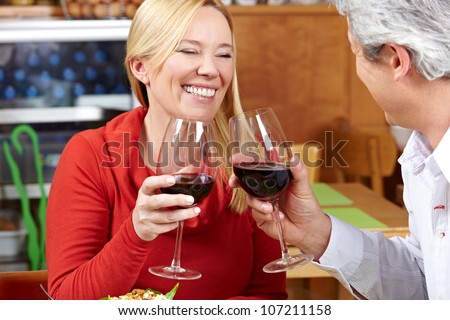 Elderly couple in restaurant cheering with red wine