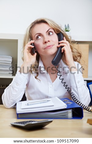 Stressed business woman in the office using two phones simultaneously