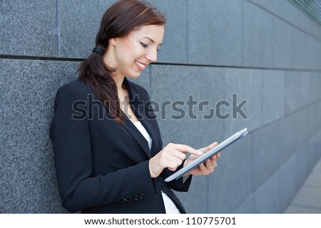 Urban business woman using tablet computer while leaning on wall