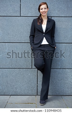 Content happy business woman in city leaning on wall