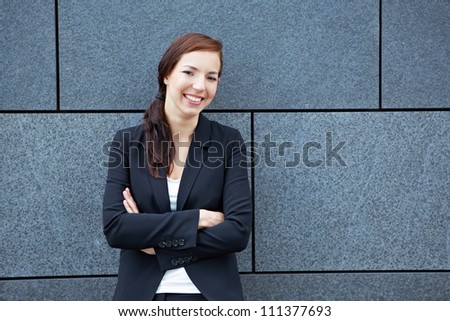 Happy business woman with her arms crossed leaning on a wall