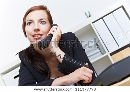 Smiling secretary using the phone in the office for a call