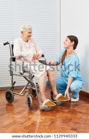 Nursing lady helps elderly woman to put on slippers in nursing home
