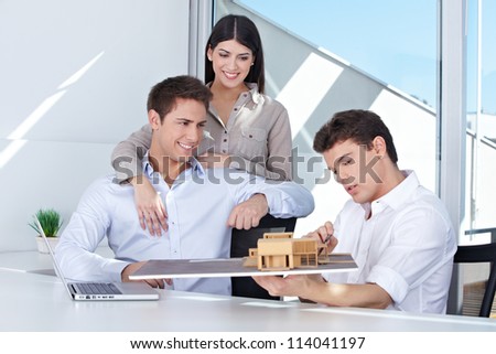 Architect showing house model to smiling couple in his office