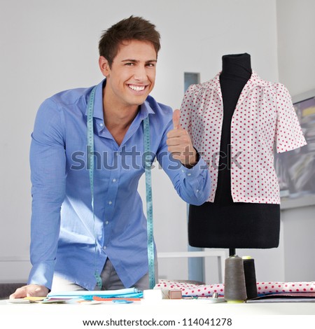 Happy tailor holding thumbs up near a dress form