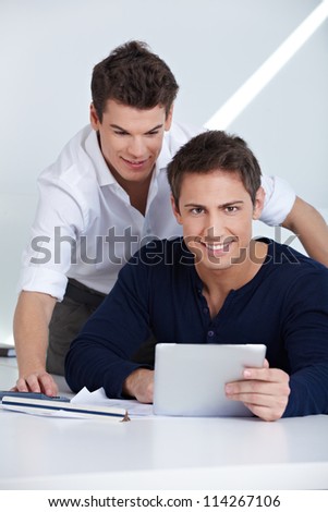 Two business people sitting with a tablet computer at their desk in the office