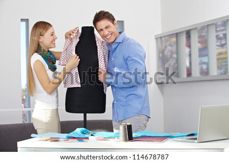 Happy man and woman in a studio dressing a dress form