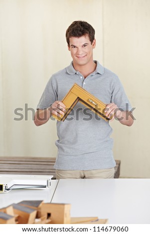 Happy carpenter holding a window frame sample in his work shop