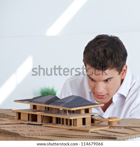 Architect in office looking at house model made of wood and cardboard