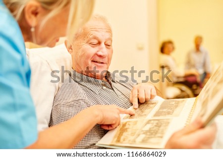Senior man with dementia looks at photos together with caregiver in nursing home