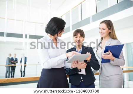Mature female professional discussing over tablet computer with smiling colleagues in office