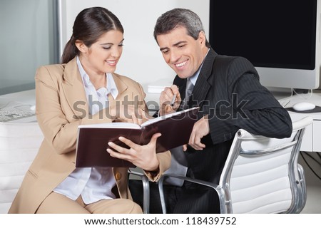 Two smiling business people looking in an appointment book in the office