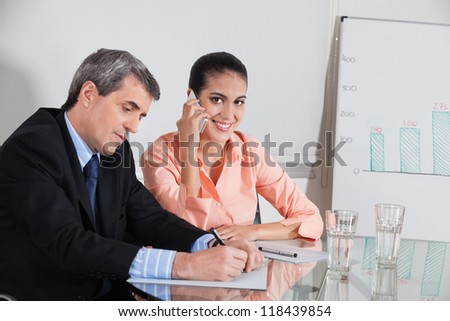 Business woman making a call in a meeting while a manager takes notes