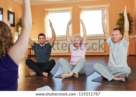Group exercising cross-legged with fitness trainer in a health club
