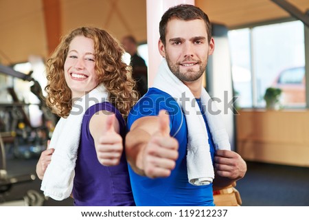 Happy smiling young couple in health club holding their thumbs up