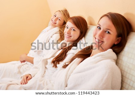 Three smiling relaxed women sitting on a heated bench after the sauna