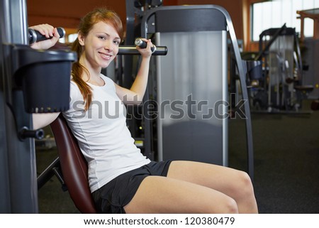 Happy woman doing exercises in sports club on a shoulder press