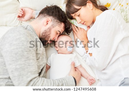 Mother and father as happy parents sleep next to their little baby
