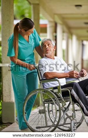 Nurse talking to elderly man in wheelchair in a nursing home