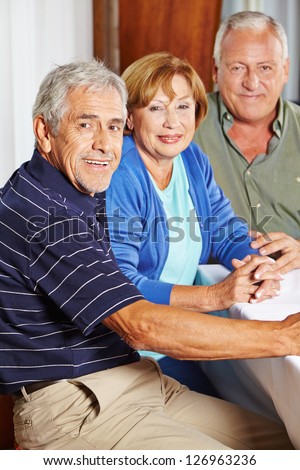 Portrait of three happy seniors sitting at table in a rest home