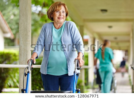 Old happy woman with walker on a stroll in the park of a nursing home