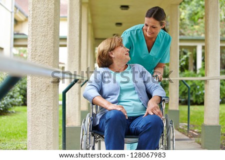 Senior Woman In Wheelchair Talking To A Nurse In A Hospital Garden